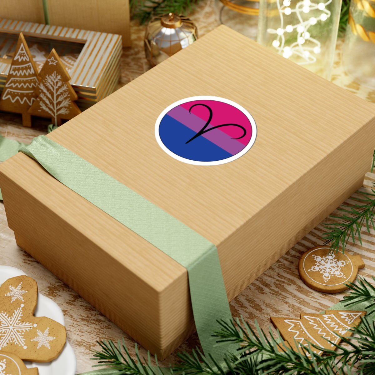 Gift box with a green ribbon on a festive background with cookies and Christmas decorations. Aires Bisexual pride sticker centered on the box.