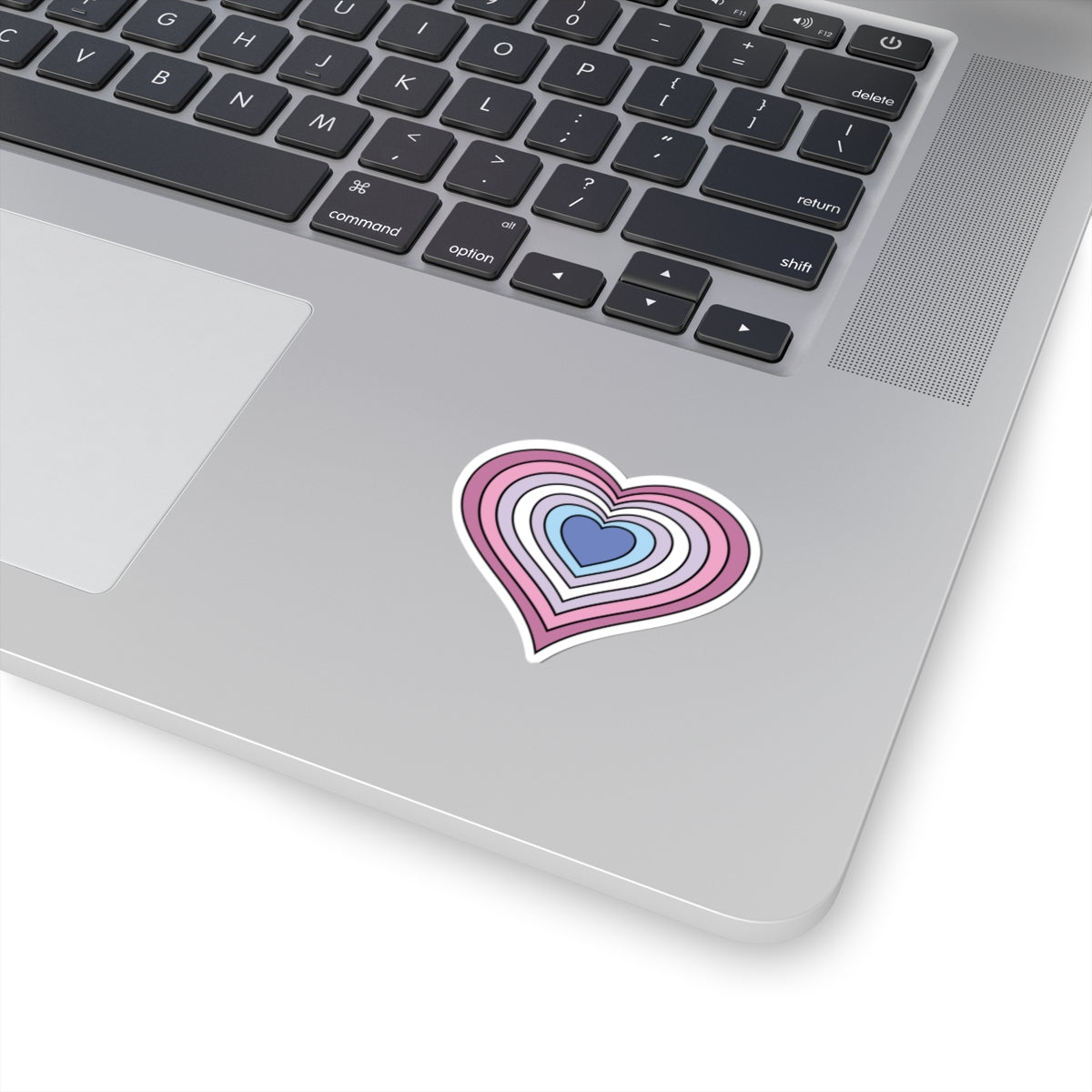 Close-up of the bottom right corner of a silver laptop featuring a 2 inch by 2 inch pride flag heart sticker in a Bigender flag style applied to the surface.