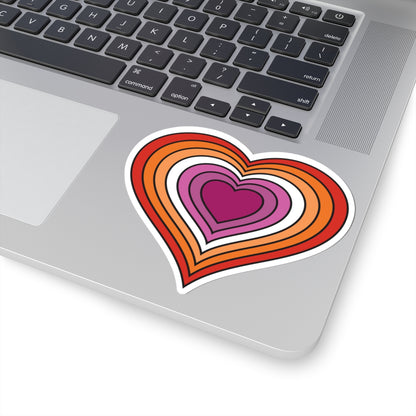 Close-up of the bottom right corner of a silver laptop featuring a 6 inches by 6 inches pride flag heart sticker in a Drag pride flag style applied to the surface.