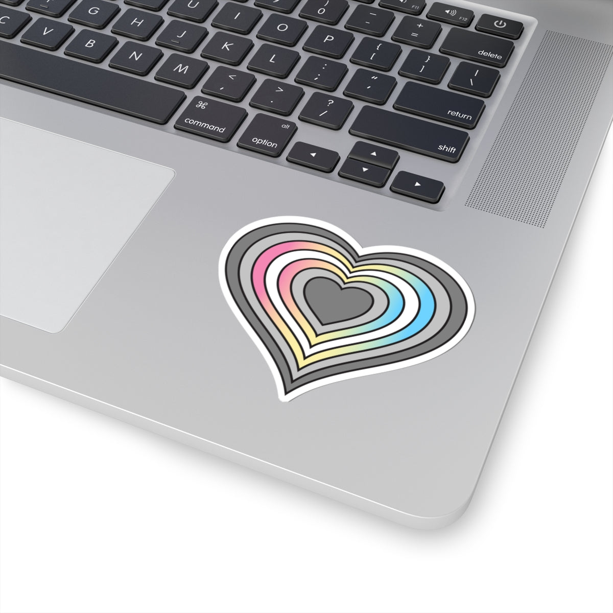 Close-up of the bottom right corner of a silver laptop featuring a 3 inch by 3 inch pride flag heart sticker in a Demifluid flag style applied to the surface.