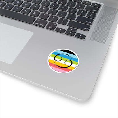 Close-up of the bottom right corner of a silver laptop featuring a 2 inch by 2 inch circular zodiac sticker with a centered Cancer glyph on a Queer pride flag style background applied to the surface.