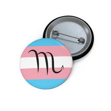 Front and back view of a circular transgender pride flag button featuring the Scorpio zodiac symbol in black centered on the front.