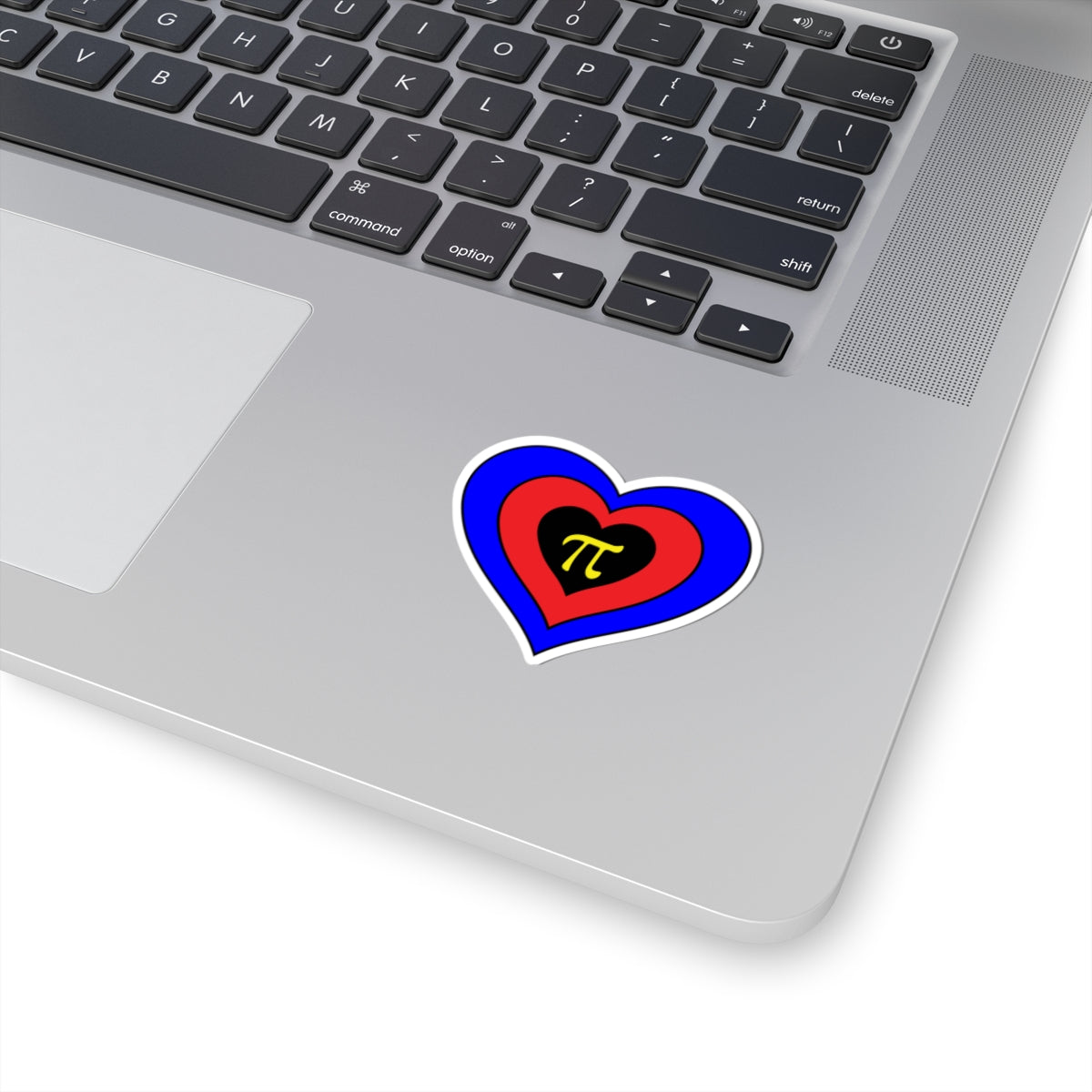 Close-up of the bottom right corner of a silver laptop featuring a 2 inch by 2 inch pride flag heart sticker in a Polyamory flag style applied to the surface.