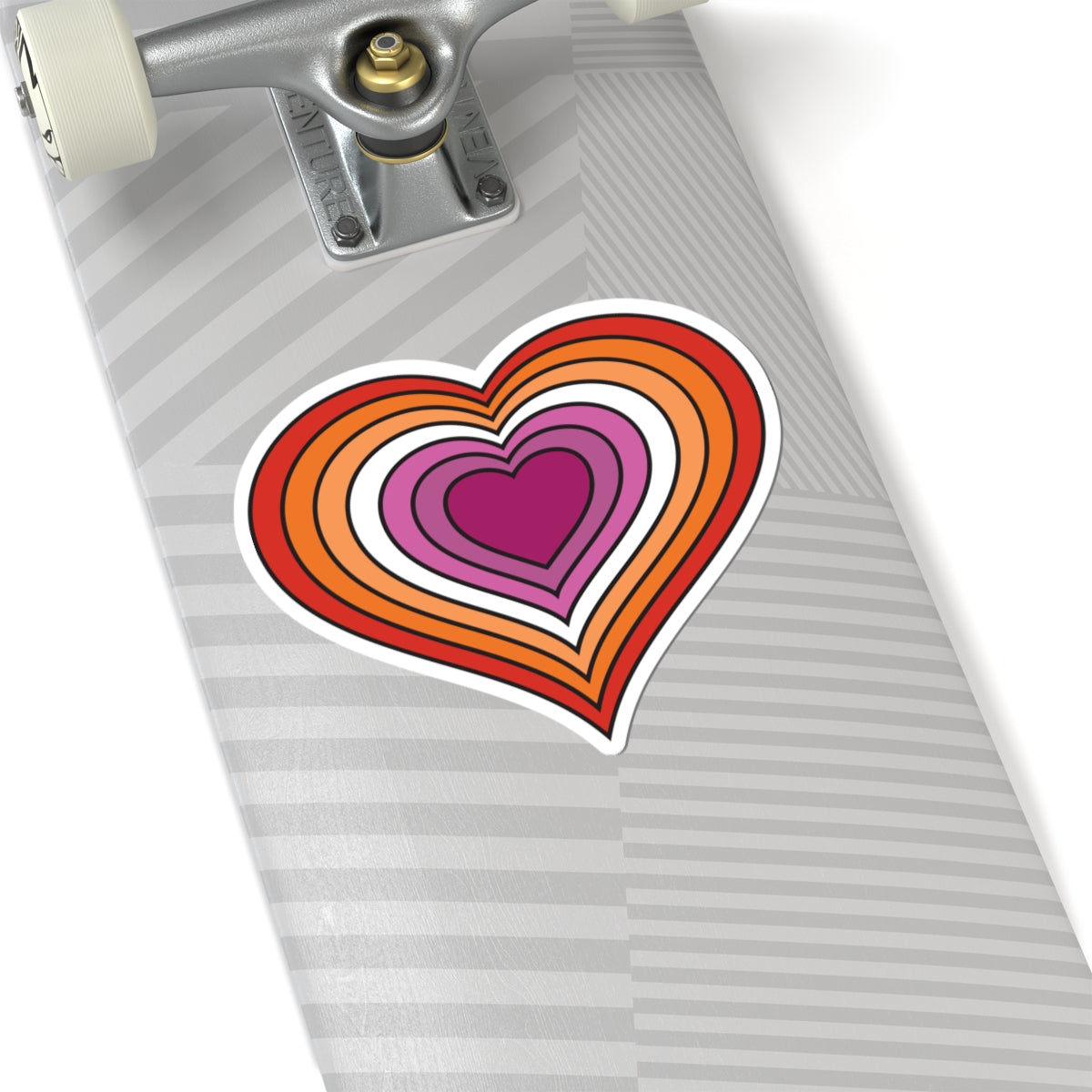 Close-up of the bottom of a silver skateboard featuring a 6 inches by 6 inches pride flag heart sticker in a Lesbian pride flag style applied to the surface.