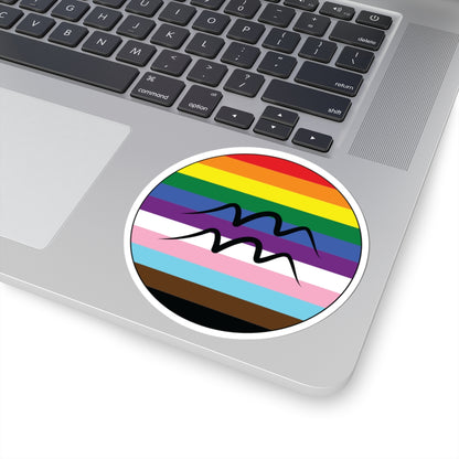 Close-up of the bottom right corner of a silver laptop featuring a 4 inch by 4 inch circular zodiac sticker with a centered Aquarius glyph on a progress pride flag style background applied to the surface.