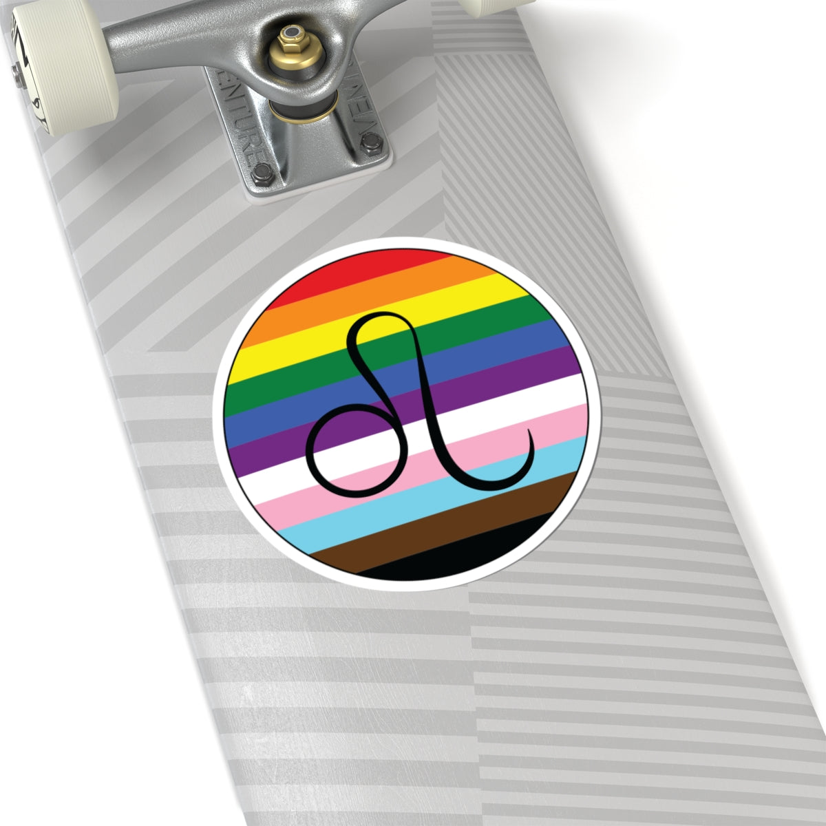 Close-up of the bottom of a silver skateboard featuring a 6 inch by 6 inch circular zodiac sticker with a centered Leo glyph on a progress pride flag style background applied to the surface.