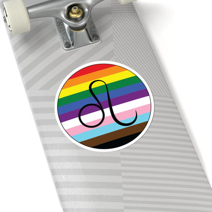 Close-up of the bottom of a silver skateboard featuring a 6 inch by 6 inch circular zodiac sticker with a centered Leo glyph on a progress pride flag style background applied to the surface.
