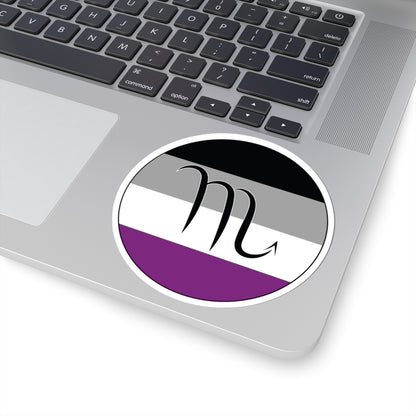 Close-up of the bottom right corner of a silver laptop featuring a 4 inch by 4 inch circular zodiac sticker with a centered Scorpio glyph on an Asexual pride flag style background applied to the surface.