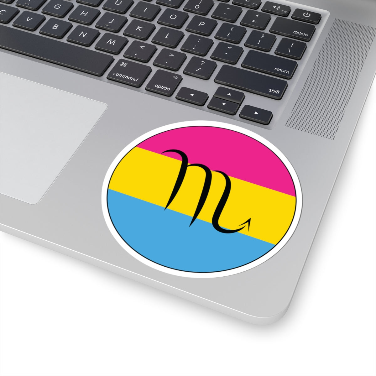 Close-up of the bottom right corner of a silver laptop featuring a 4 inch by 4 inch circular zodiac sticker with a centered Scorpio glyph on a Pansexual pride flag style background applied to the surface.