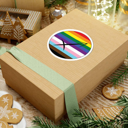 Gift box with a green ribbon on a festive background with cookies and Christmas decorations. Sagittarius Progress pride sticker centered on the box.