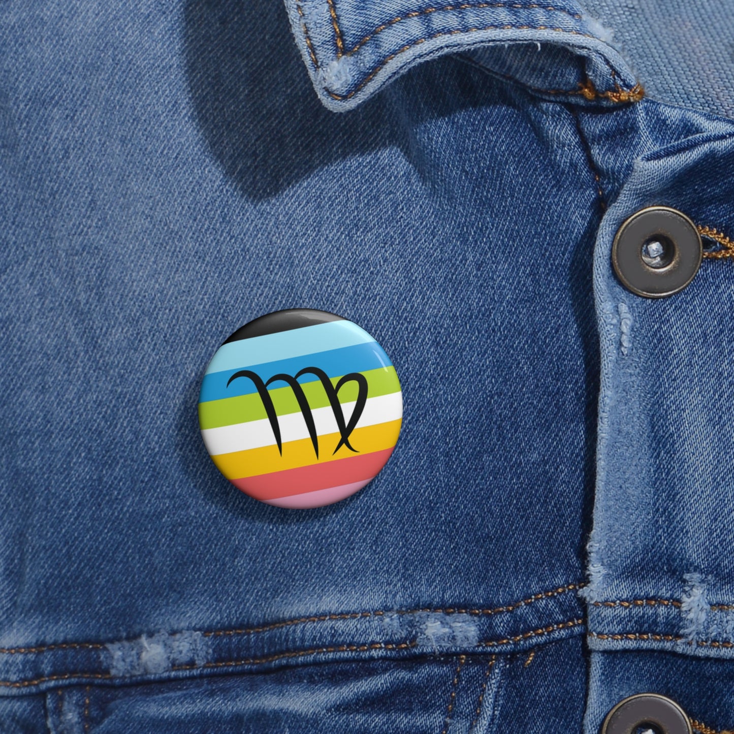 Close-up of a white circular pride button featuring the Virgo zodiac glyph centered over a queer pride flag background in pinks, yellow, white, green, blues, and black, attached to a blue denim jacket at the right chest with the button clearly visible.