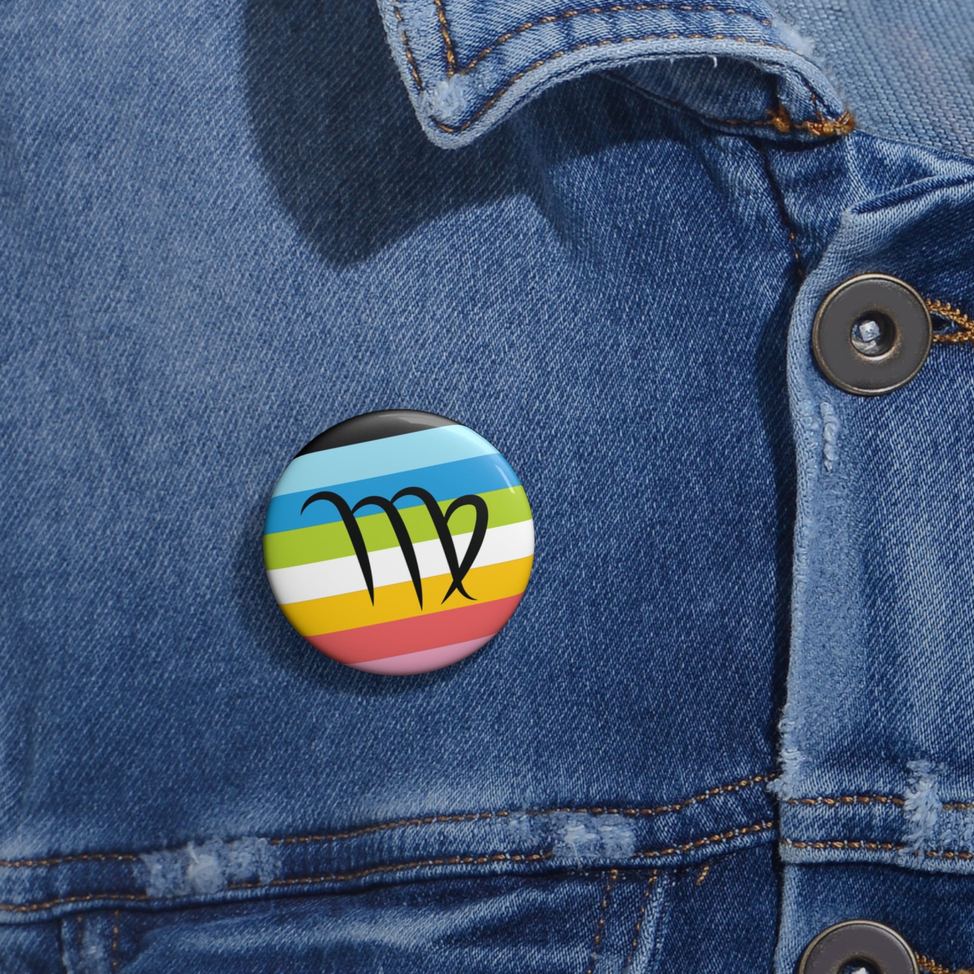 Close-up of a white circular pride button featuring the Virgo zodiac glyph centered over a queer pride flag background in pinks, yellow, white, green, blues, and black, attached to a blue denim jacket at the right chest with the button clearly visible.
