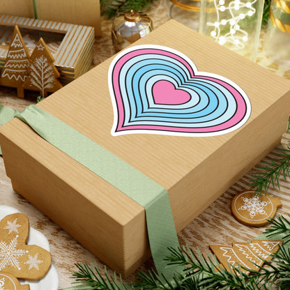 Gift box with a green ribbon on a festive background with cookies and Christmas decorations. Heart-shaped Transmasc pride sticker centered on the box.