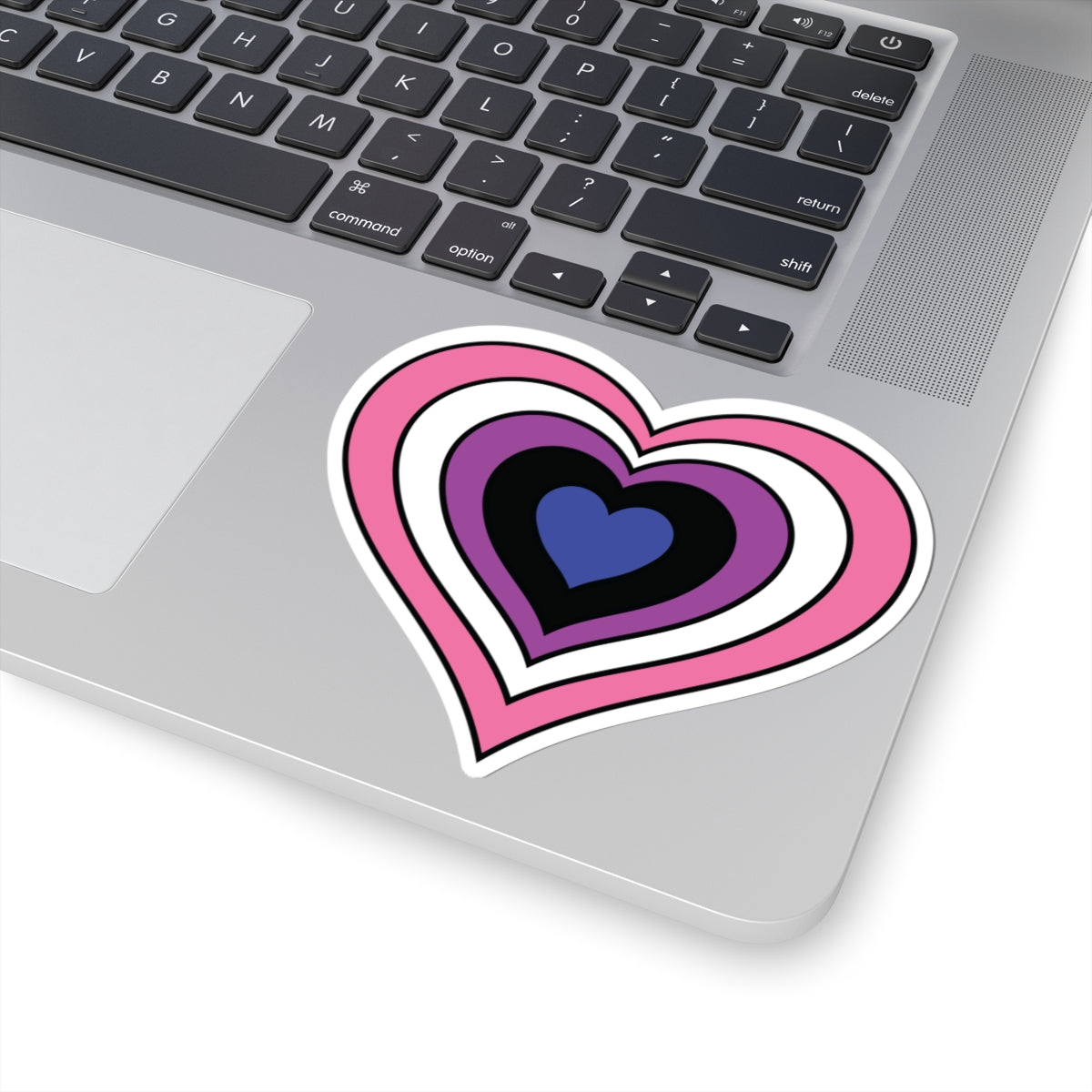 Close-up of the bottom right corner of a silver laptop featuring a 4 inch by 4 inch pride flag heart sticker in a Genderfluid flag style applied to the surface.