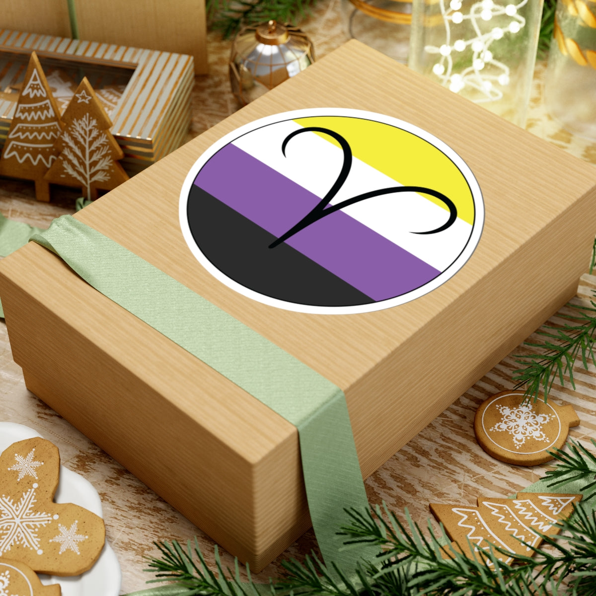Gift box with a green ribbon on a festive background with cookies and Christmas decorations. Aires Nonbinary pride sticker centered on the box.