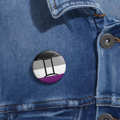 Close-up of a white circular pride button featuring the Gemini zodiac glyph centered over an asexual pride flag background in black, gray, white, and purple, attached to a blue denim jacket at the right chest with the button clearly visible.