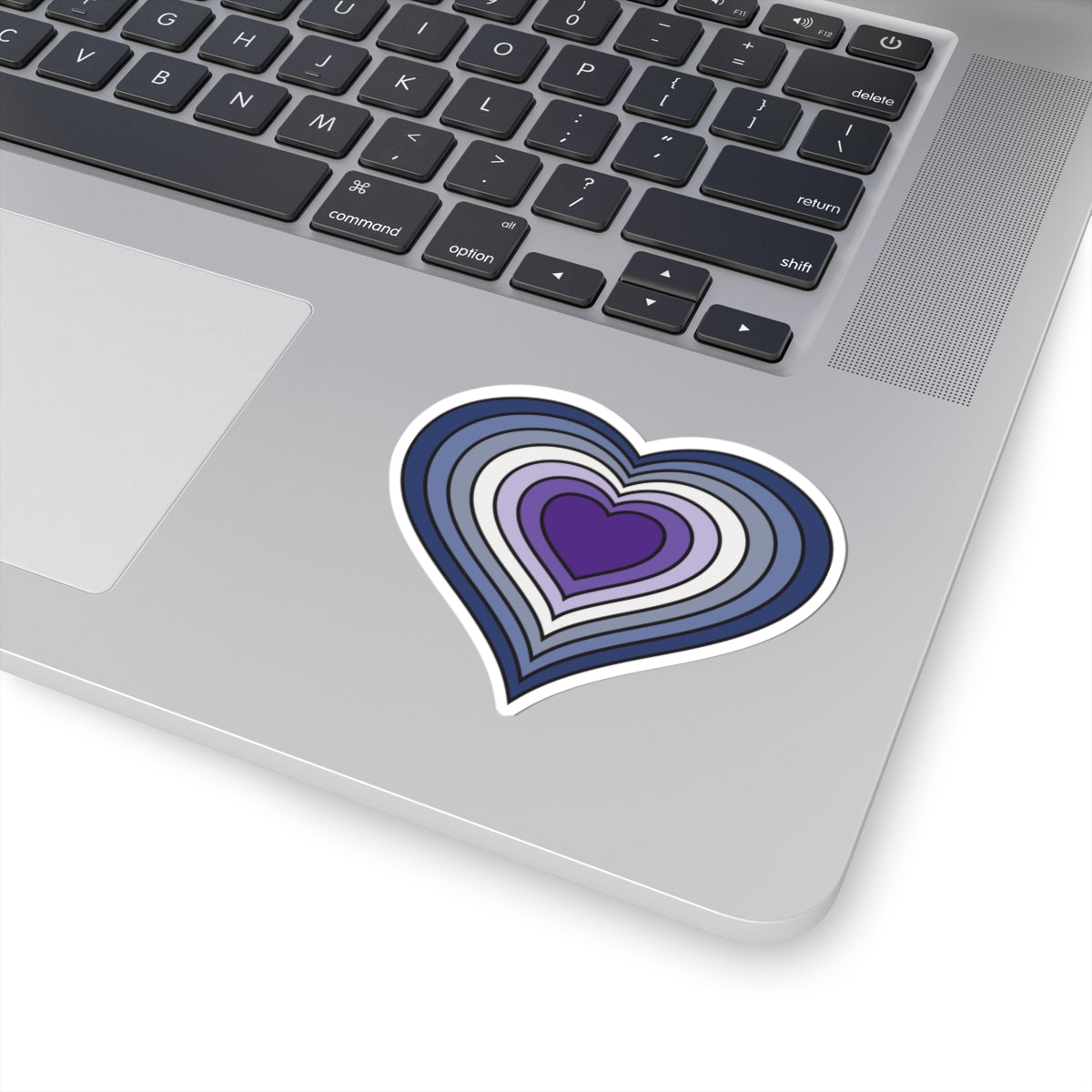 Close-up of the bottom right corner of a silver laptop featuring a 3 inch by 3 inch pride flag heart sticker in a purple butch pride flag style applied to the surface.