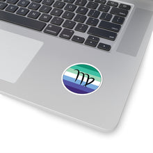 Close-up of the bottom right corner of a silver laptop featuring a 2 inch by 2 inch circular zodiac sticker with a centered Virgo glyph on a Gay Men pride flag style background applied to the surface.