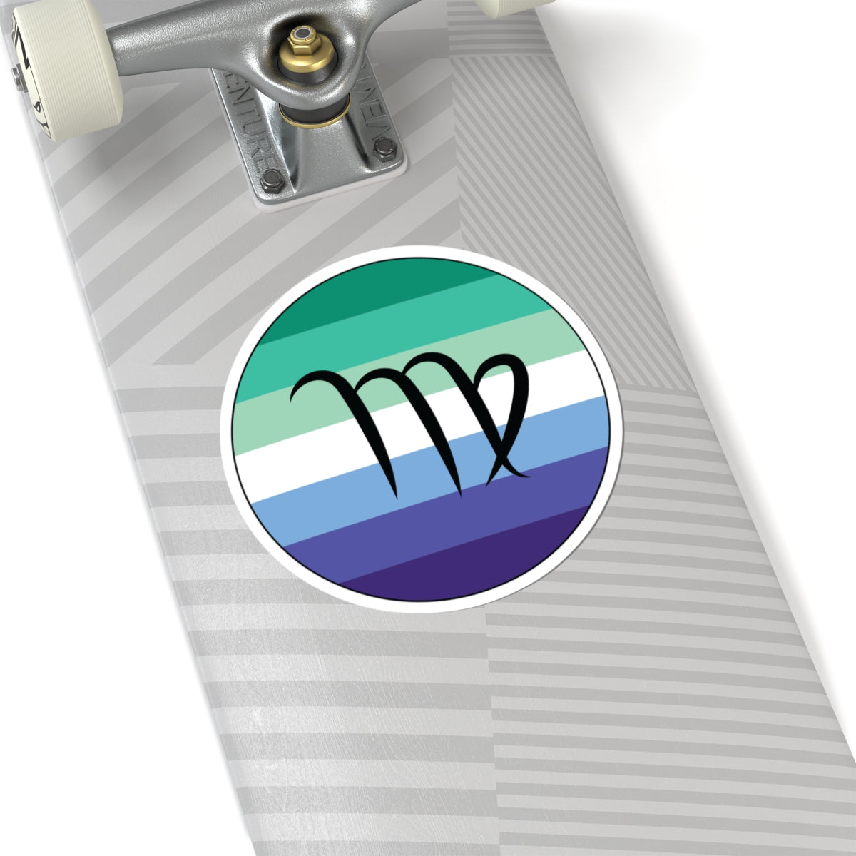 Close-up of the bottom of a silver skateboard featuring a 6 inch by 6 inch circular zodiac sticker with a centered Virgo glyph on a Gay Men pride flag style background applied to the surface.