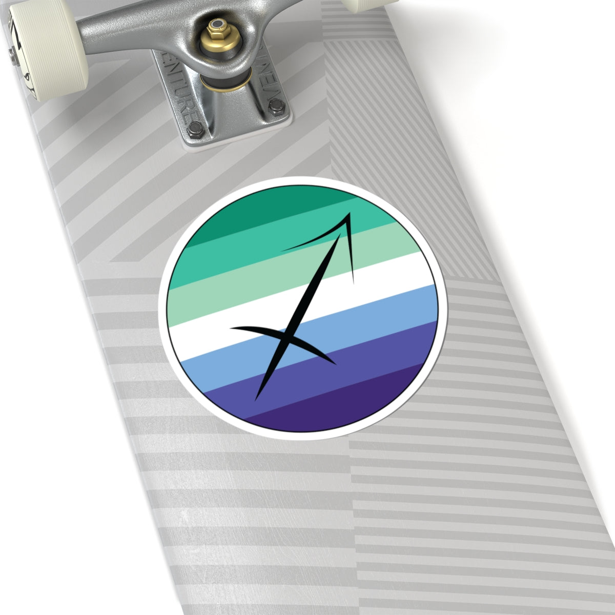 Close-up of the bottom of a silver skateboard featuring a 6 inch by 6 inch circular zodiac sticker with a centered Sagittarius glyph on a Gay Men pride flag style background applied to the surface.