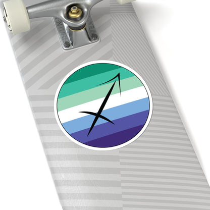 Close-up of the bottom of a silver skateboard featuring a 6 inch by 6 inch circular zodiac sticker with a centered Sagittarius glyph on a Gay Men pride flag style background applied to the surface.
