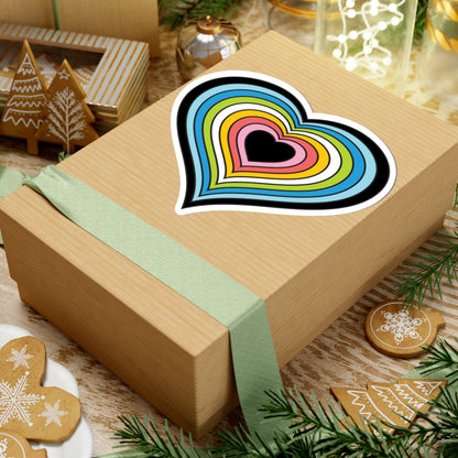 Gift box with a green ribbon on a festive background with cookies and Christmas decorations. Heart-shaped Queer pride sticker centered on the box.