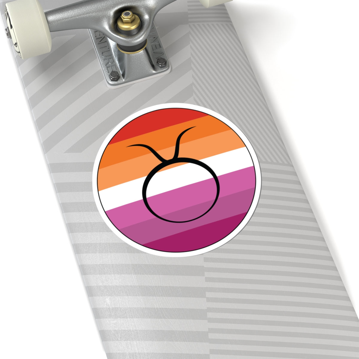 Close-up of the bottom of a silver skateboard featuring a 6 inch by 6 inch circular zodiac sticker with a centered Taurus glyph on a Lesbian pride flag style background applied to the surface.