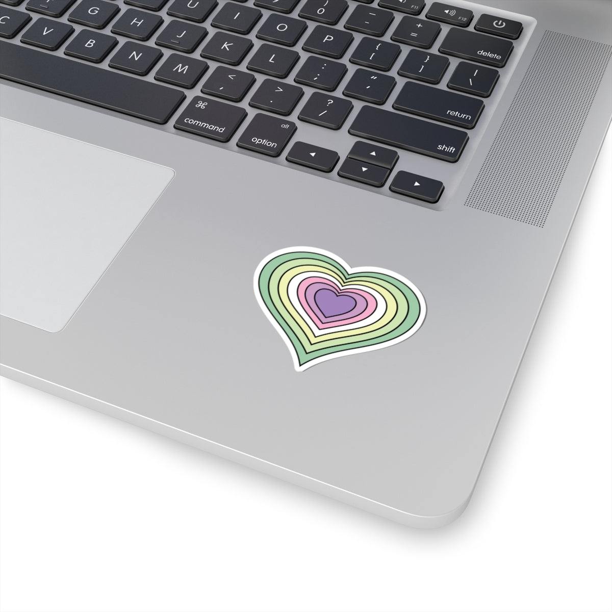 Close-up of the bottom right corner of a silver laptop featuring a 2 inch by 2 inch pride flag heart sticker in a Genderfae flag style applied to the surface.
