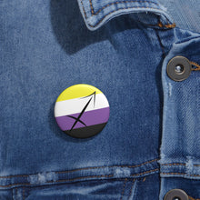 Close-up of a white circular pride button featuring the Sagittarius zodiac glyph centered over a nonbinary pride flag background in yellow, white, purple, and black, attached to a blue denim jacket at the right chest with the button clearly visible.