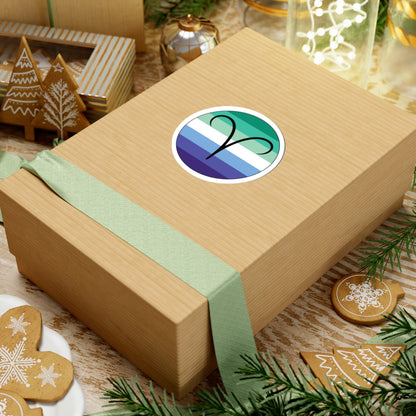 Gift box with a green ribbon on a festive background with cookies and Christmas decorations. Aires Gay Men pride sticker centered on the box.