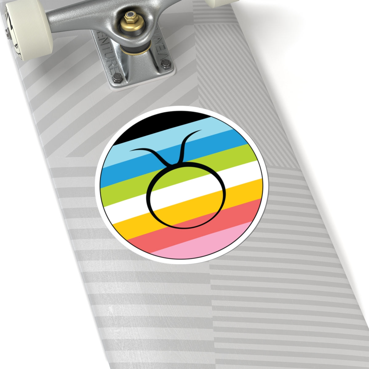 Close-up of the bottom of a silver skateboard featuring a 6 inch by 6 inch circular zodiac sticker with a centered Taurus glyph on a Queer pride flag style background applied to the surface.