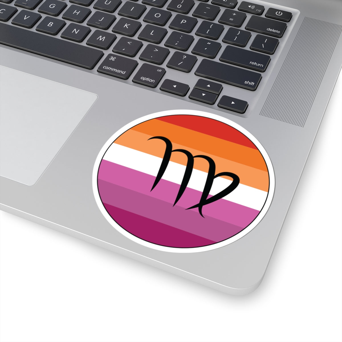 Close-up of the bottom right corner of a silver laptop featuring a 4 inch by 4 inch circular zodiac sticker with a centered Virgo glyph on a Lesbian pride flag style background applied to the surface.