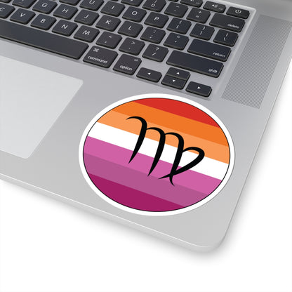 Close-up of the bottom right corner of a silver laptop featuring a 4 inch by 4 inch circular zodiac sticker with a centered Virgo glyph on a Lesbian pride flag style background applied to the surface.