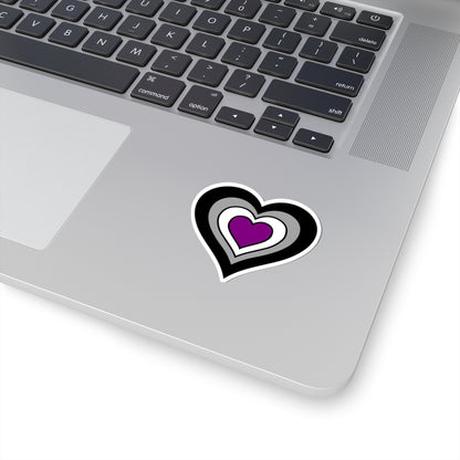 Close-up of the bottom right corner of a silver laptop featuring a 2 inch by 2 inch pride flag heart sticker in an Asexual flag style applied to the surface.