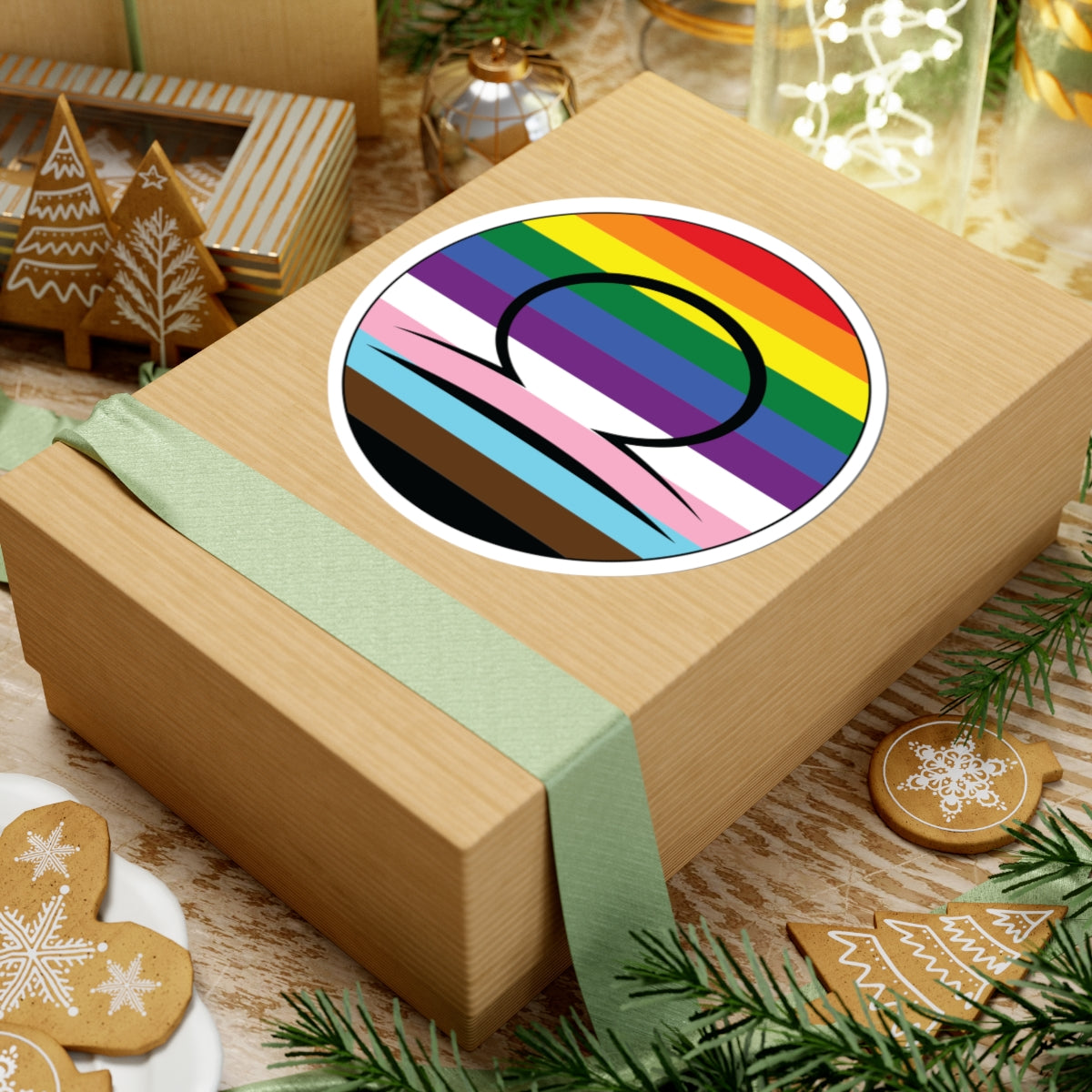 Gift box with a green ribbon on a festive background with cookies and Christmas decorations. Libra Progress pride sticker centered on the box.