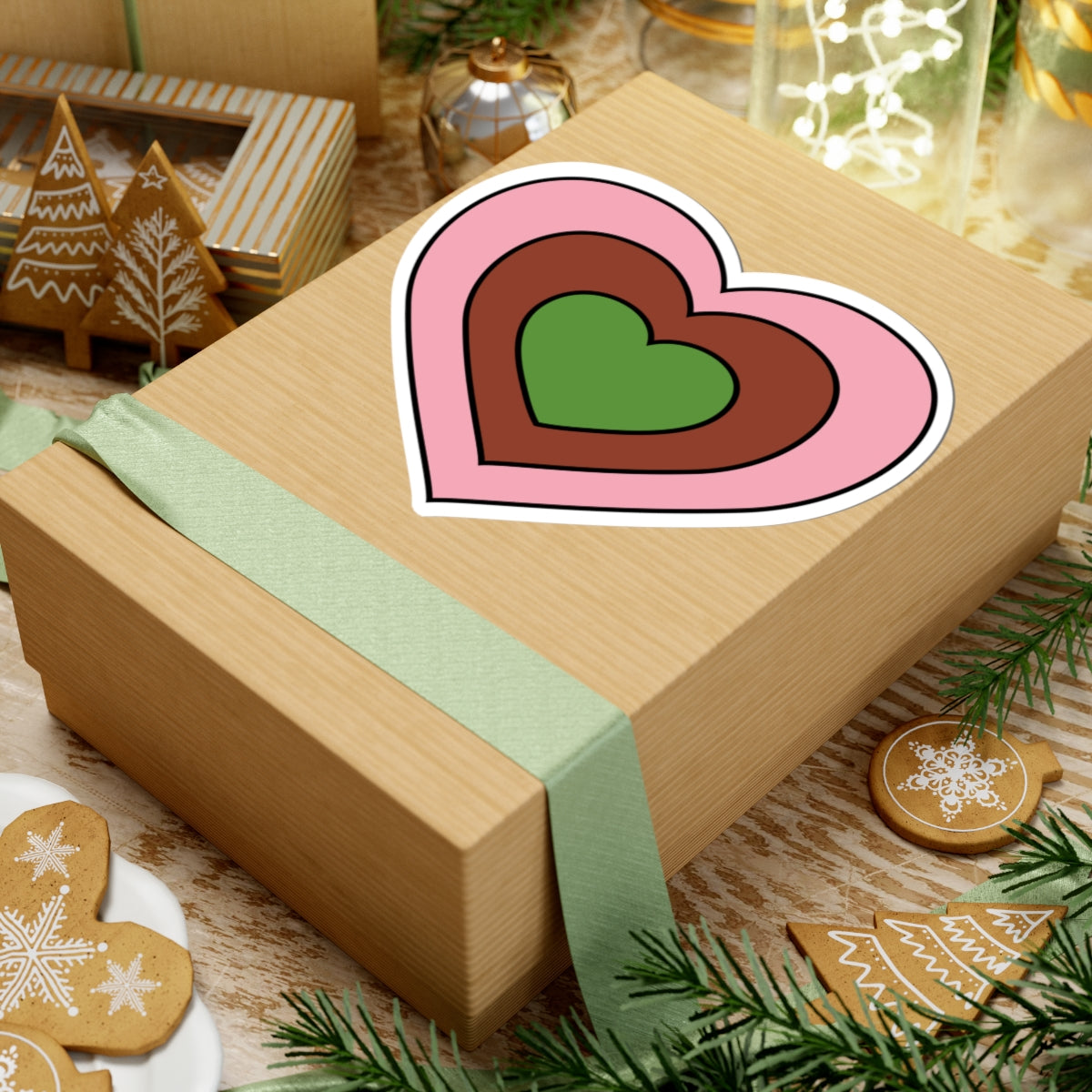 Gift box with a green ribbon on a festive background with cookies and Christmas decorations. Heart-shaped Gynesexual pride sticker centered on the box.