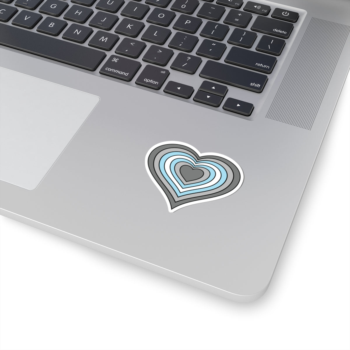Close-up of the bottom right corner of a silver laptop featuring a 2 inch by 2 inch pride flag heart sticker in a Demiboy flag style applied to the surface.