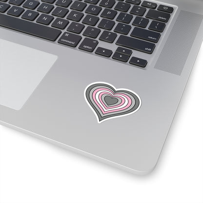 Close-up of the bottom right corner of a silver laptop featuring a 2 inch by 2 inch pride flag heart sticker in a Demigirl flag style applied to the surface.