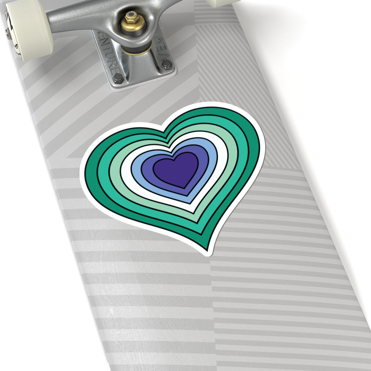 Close-up of the bottom of a silver skateboard featuring a 2 inch by 2 inch pride flag heart sticker in a Gay Men flag style applied to the surface.
