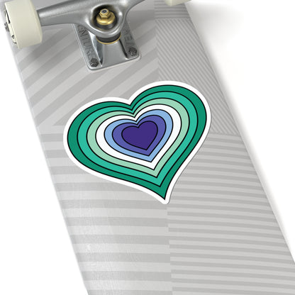 Close-up of the bottom of a silver skateboard featuring a 2 inch by 2 inch pride flag heart sticker in a Gay Men flag style applied to the surface.