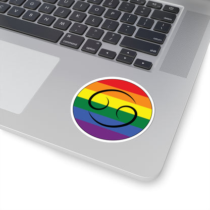 Close-up of the bottom right corner of a silver laptop featuring a 3 inch by 3 inch circular zodiac sticker with a centered Cancer glyph on a Rainbow pride flag style background applied to the surface.