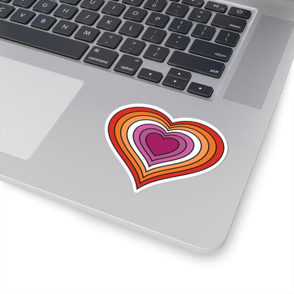 Close-up of the bottom right corner of a silver laptop featuring a 4 inches by 4 inches pride flag heart sticker in a Lesbian pride flag style applied to the surface.