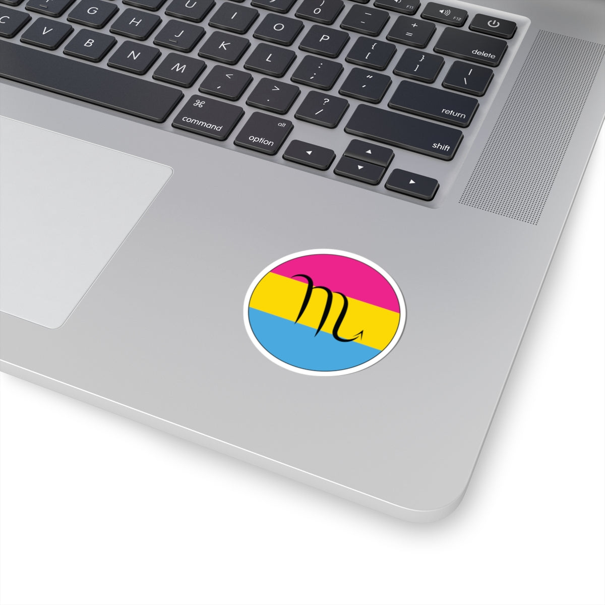 Close-up of the bottom right corner of a silver laptop featuring a 2 inch by 2 inch circular zodiac sticker with a centered Scorpio glyph on a Pansexual pride flag style background applied to the surface.