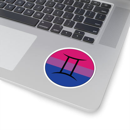 Close-up of the bottom right corner of a silver laptop featuring a 3 inch by 3 inch circular zodiac sticker with a centered Gemini glyph on a Bisexual pride flag style background applied to the surface.