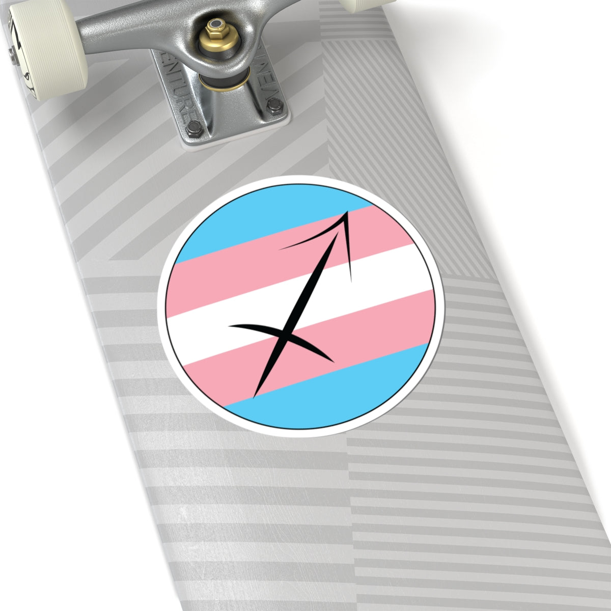 Close-up of the bottom of a silver skateboard featuring a 6 inch by 6 inch circular zodiac sticker with a centered Capricorn glyph on a Transgender pride flag style background applied to the surface.