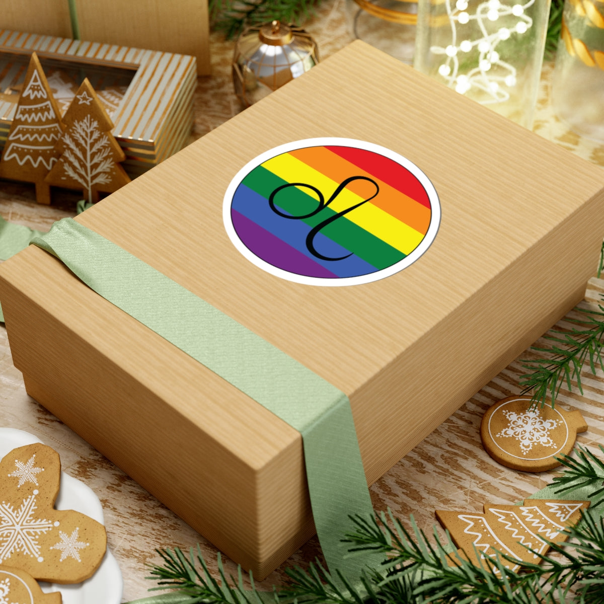 Gift box with a green ribbon on a festive background with cookies and Christmas decorations. Leo Rainbow pride sticker centered on the box.