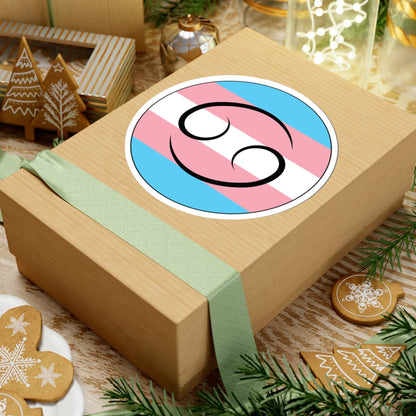 Gift box with a green ribbon on a festive background with cookies and Christmas decorations. Cancer Transgender pride sticker centered on the box.