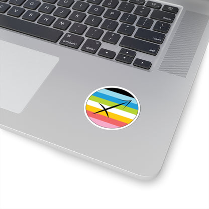 Close-up of the bottom right corner of a silver laptop featuring a 2 inch by 2 inch circular zodiac sticker with a centered Sagittarius glyph on a Queer pride flag style background applied to the surface.