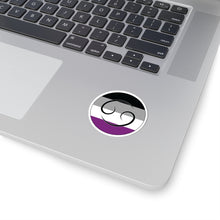 Close-up of the bottom right corner of a silver laptop featuring a 2 inch by 2 inch circular zodiac sticker with a centered Cancer glyph on an Asexual pride flag style background applied to the surface.