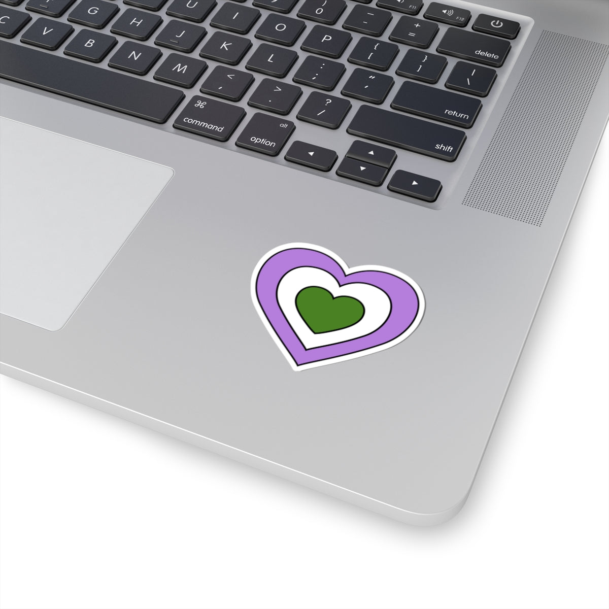 Close-up of the bottom right corner of a silver laptop featuring a 2 inch by 2 inch pride flag heart sticker in a Genderqueer flag style applied to the surface.
